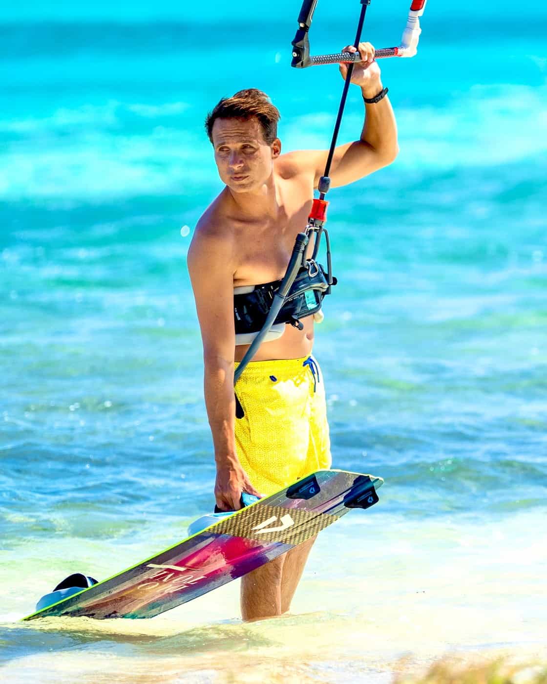 Jeremie Tronet holding his kiteboard in shallow water on Union Island